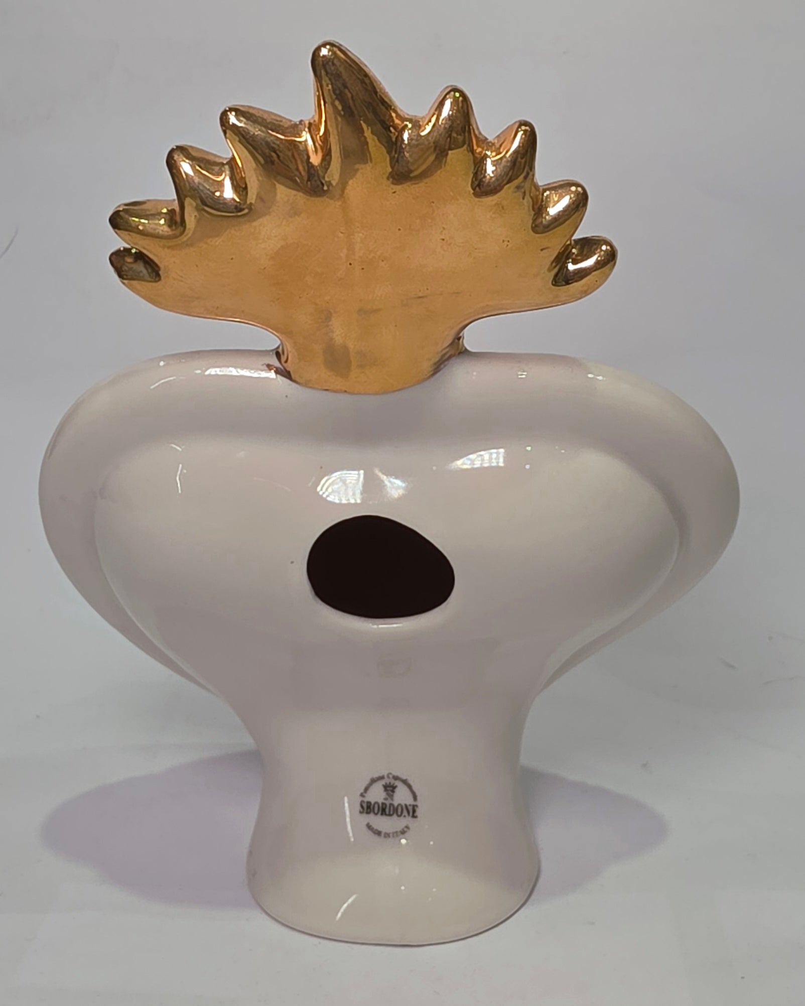 Scultura a forma di Cuore Sacro in ceramica rossa lucida, completata da una fiamma superiore dorata e una cornice bianca perlinata con borchie oro. Questo oggetto di design artigianale con base d'appoggio è un complemento d'arredo iconico, ideale per donare un tocco di eleganza e spiritualità moderna agli interni.