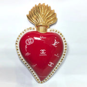 Scultura da parete a forma di Cuore Sacro grande in ceramica rossa lucida, decorata con diversi loghi fashion bianchi e sormontata da una fiamma dorata a rilievo. L'oggetto è rifinito con una cornice perlinata bianca e borchie oro, rappresentando un complemento d'arredo pop art dal design audace ideale per ambienti moderni.