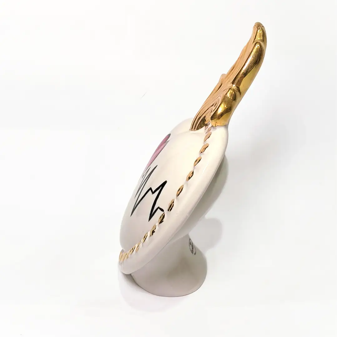 Scultura decorativa a forma di Cuore Sacro in ceramica bianca lucida, caratterizzata da un cuore rosso centrale sovrapposto a un disegno grafico nero che richiama il battito cardiaco. L'oggetto è impreziosito da una fiamma superiore dorata e una cornice perlinata con borchie oro, rendendolo un complemento d'arredo dal design moderno e originale.
