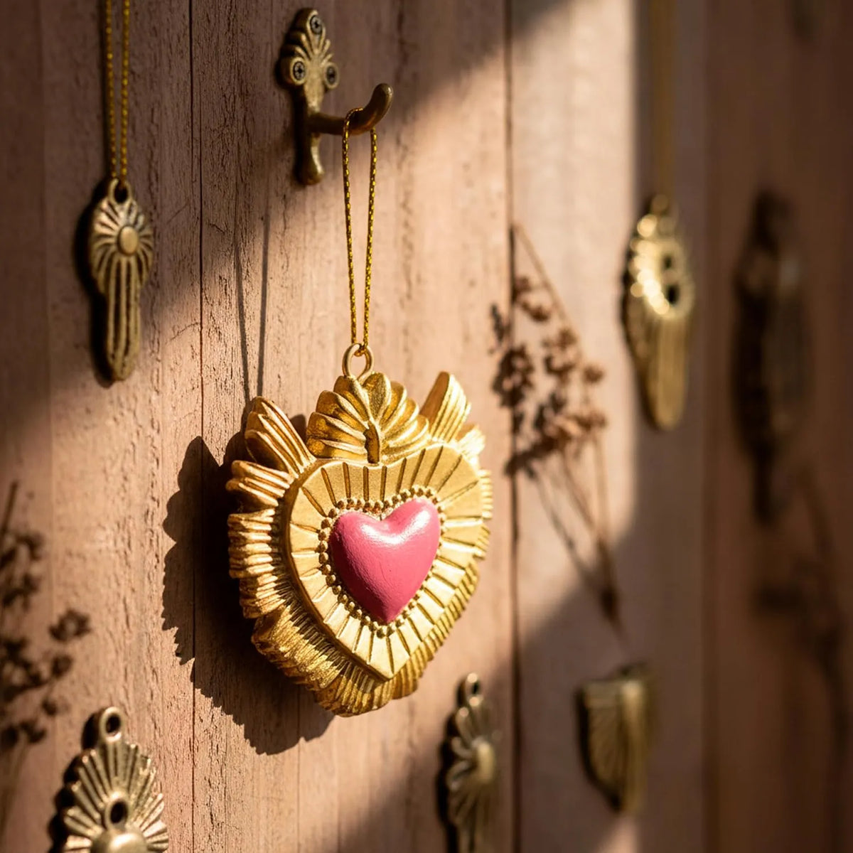 Ciondolo decorativo a forma di cuore sacro votivo, con cornice dorata a motivi barocchi e fiamma superiore, centro smaltato fucsia e nastro dorato per appenderlo, misure 5x5 cm. Decoro portafortuna artigianale firmato Montemaggi, ideale come ornamento per l'albero o idea regalo originale.
