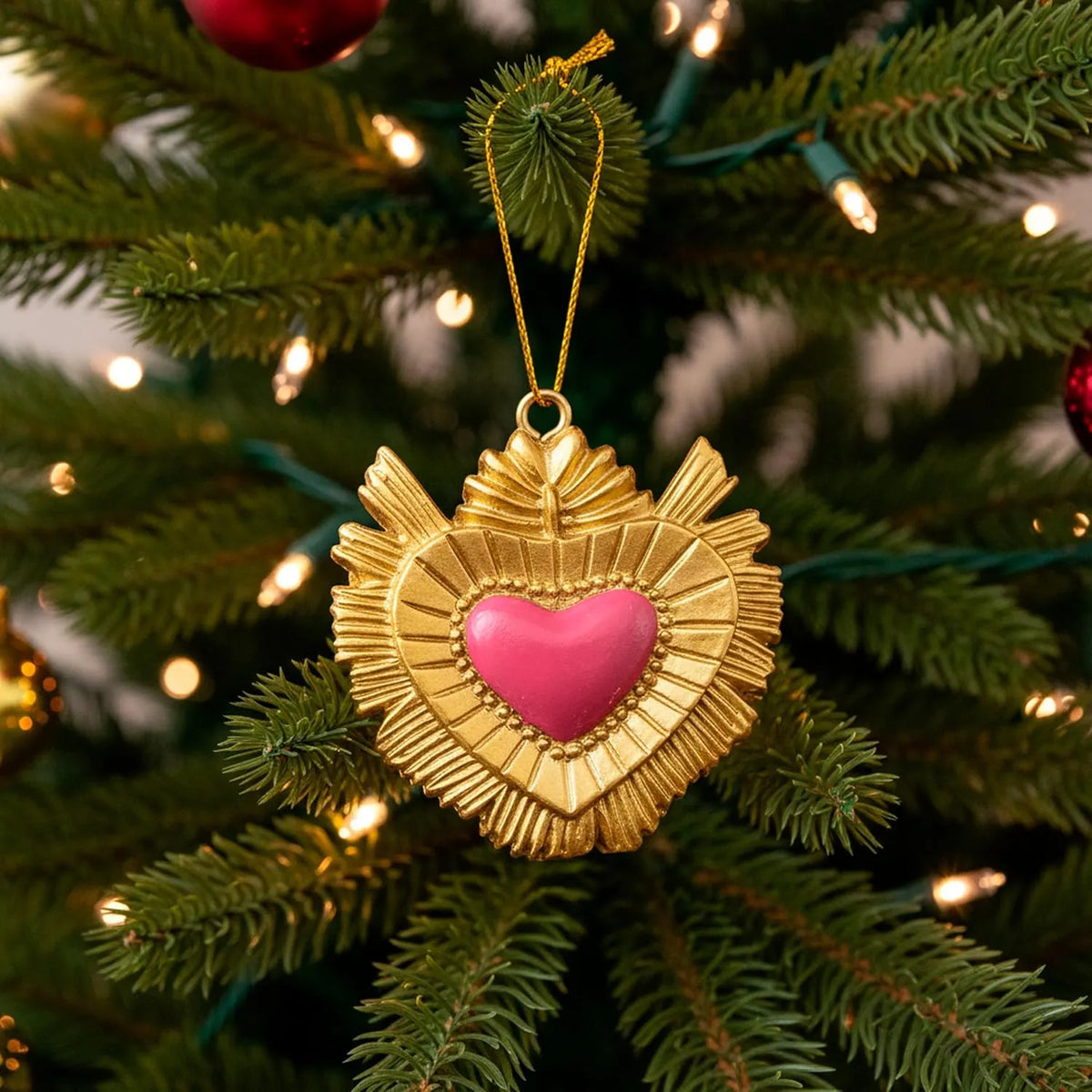 Ciondolo decorativo a forma di cuore sacro votivo, con cornice dorata a motivi barocchi e fiamma superiore, centro smaltato fucsia e nastro dorato per appenderlo, misure 5x5 cm. Decoro portafortuna artigianale firmato Montemaggi, ideale come ornamento per l'albero o idea regalo originale.