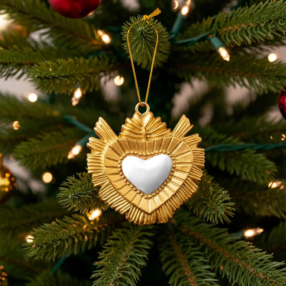 Ciondolo decorativo a forma di cuore sacro votivo, con cornice dorata a motivi barocchi e fiamma superiore, centro smaltato bianco e nastro dorato per appenderlo, misure 5x5 cm. Decoro portafortuna artigianale firmato Montemaggi, ideale come ornamento per l'albero o idea regalo originale.