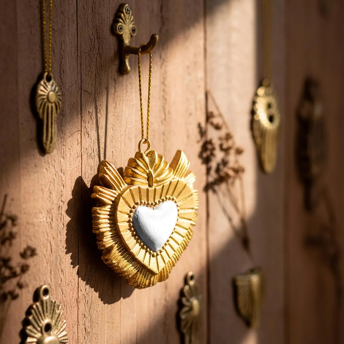 Ciondolo decorativo a forma di cuore sacro votivo, con cornice dorata a motivi barocchi e fiamma superiore, centro smaltato bianco e nastro dorato per appenderlo, misure 5x5 cm. Decoro portafortuna artigianale firmato Montemaggi, ideale come ornamento per l'albero o idea regalo originale.