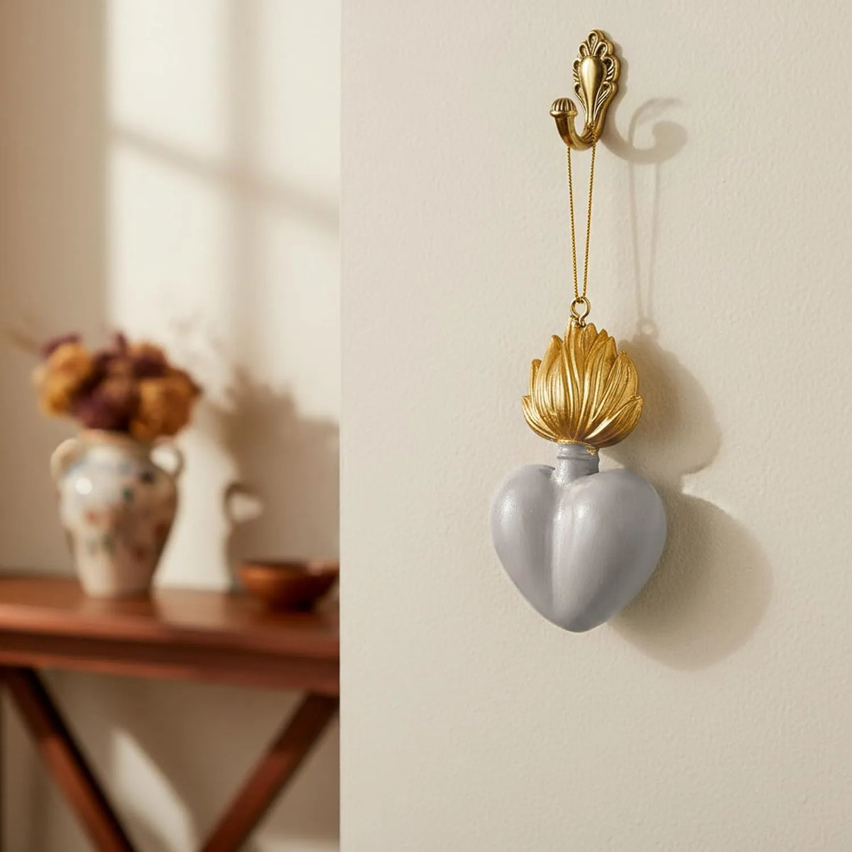 Ciondolo decorativo a forma di cuore sacro votivo, con fiamma dorata superiore, centro smaltato bianco e nastro dorato per appenderlo, misure 9x5.5 cm. Decoro portafortuna artigianale firmato Montemaggi, ideale come ornamento per l'albero o idea regalo originale.
