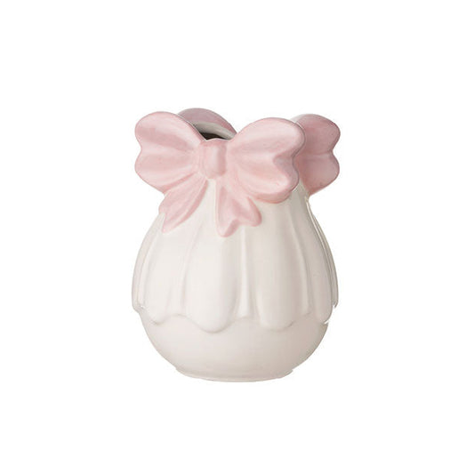 Vaso tondo in ceramica bianca del marchio L'arte dei nacchi con una struttura bombata alla base e una lavorazione a rilievo che richiama i petali di un fiore o una superficie plissettata. L'imboccatura è decorata da un grande fiocco rosa tridimensionale che funge da orlo, caratterizzato da forme morbide e una colorazione pastello delicata, perfetto come elemento d'arredo shabby chic, portaoggetti o bomboniera decorativa per cerimonie.