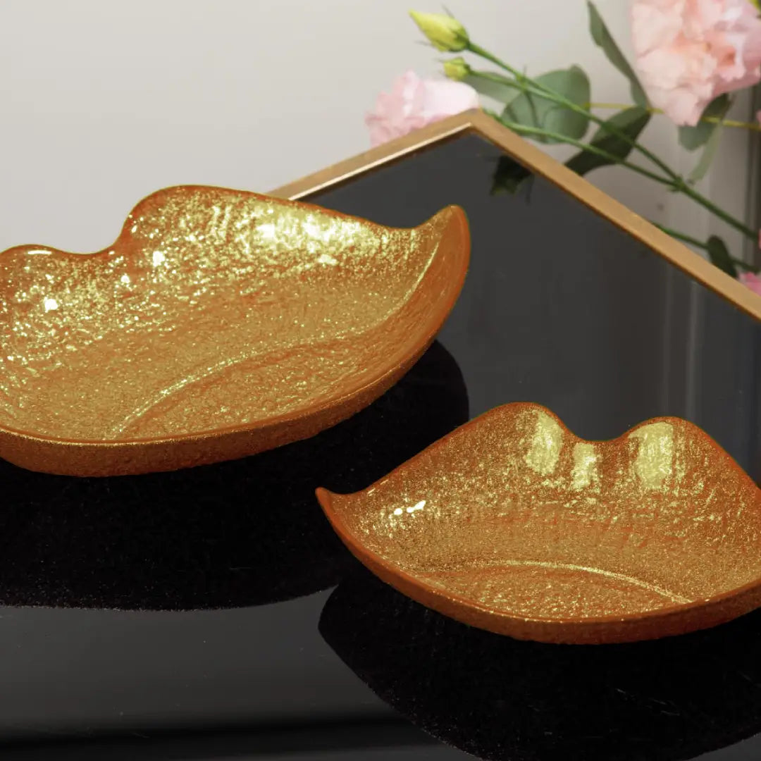 Vassoio svuotatasche a forma di bocca firmato Ilary Queen, caratterizzato da un design a labbra sagomate con una suggestiva superficie texturizzata dall'effetto glitterato e metallico. Disponibile in diverse varianti di colore assortite tra cui oro scintillante, verde smeraldo e rosso rubino, questo elegante e moderno oggetto decorativo è perfetto come svuotatasche da ingresso o come originale idea regalo per la casa.