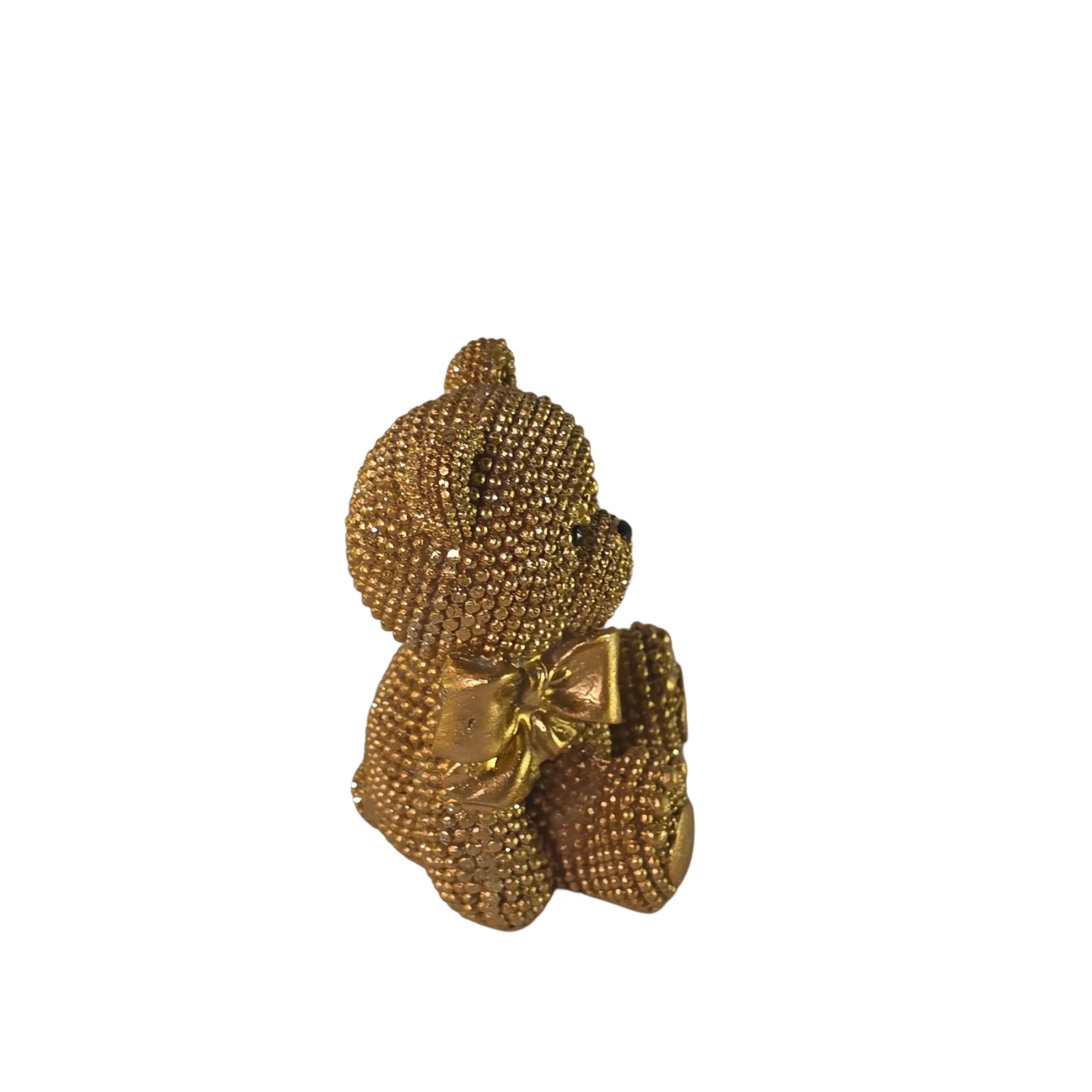 Statuina orsetto in resina dorata interamente ricoperta di brillantini glitterati, con fiocco raso oro al collo, occhi e naso neri e cuciture in rilievo sulle zampe. Oggetto decorativo scintillante firmato Sud Import, ideale come soprammobile glamour o idea regalo per bambini e occasioni speciali.