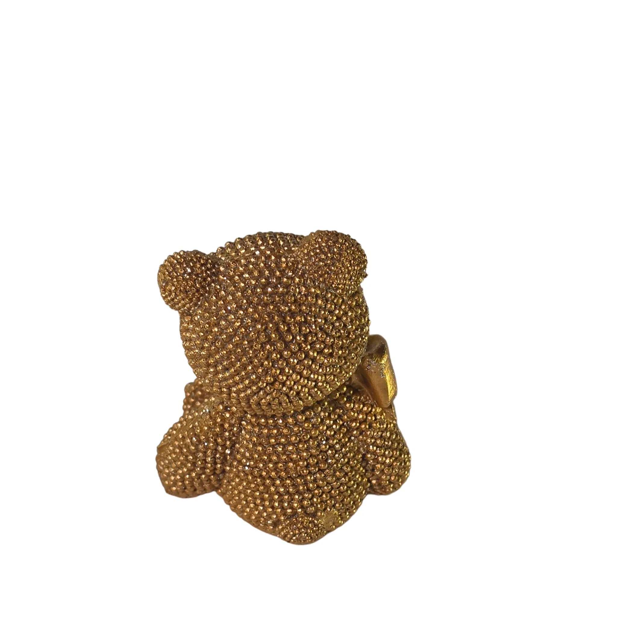 Statuina orsetto in resina dorata interamente ricoperta di brillantini glitterati, con fiocco raso oro al collo, occhi e naso neri e cuciture in rilievo sulle zampe. Oggetto decorativo scintillante firmato Sud Import, ideale come soprammobile glamour o idea regalo per bambini e occasioni speciali.