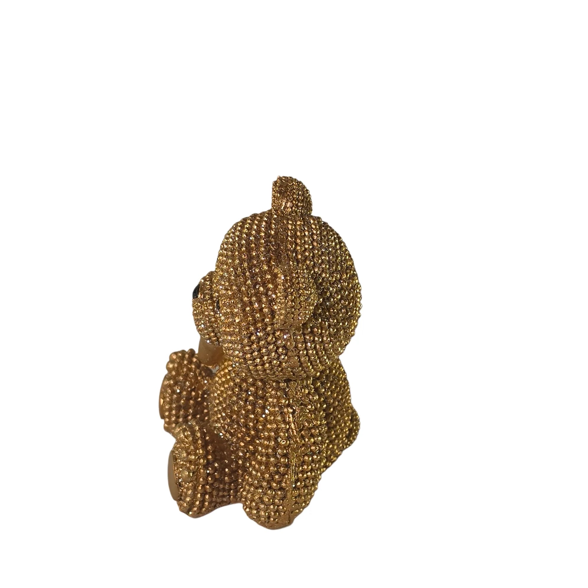 Statuina orsetto in resina dorata interamente ricoperta di brillantini glitterati, con fiocco raso oro al collo, occhi e naso neri e cuciture in rilievo sulle zampe. Oggetto decorativo scintillante firmato Sud Import, ideale come soprammobile glamour o idea regalo per bambini e occasioni speciali.