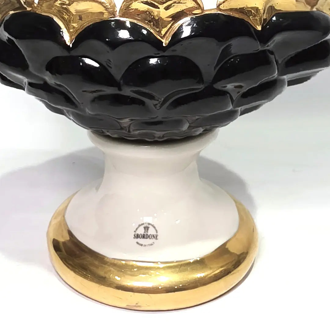 Pigna portafortuna in ceramica artigianale bicolore bianca e nera lucida, caratterizzata da una fascia centrale dorata che separa le squame in rilievo. Questo elegante oggetto ornamentale con base d'appoggio rifinita in oro è un complemento d'arredo di design ideale per donare un tocco di prestigio e tradizione siciliana agli ambienti contemporanei.