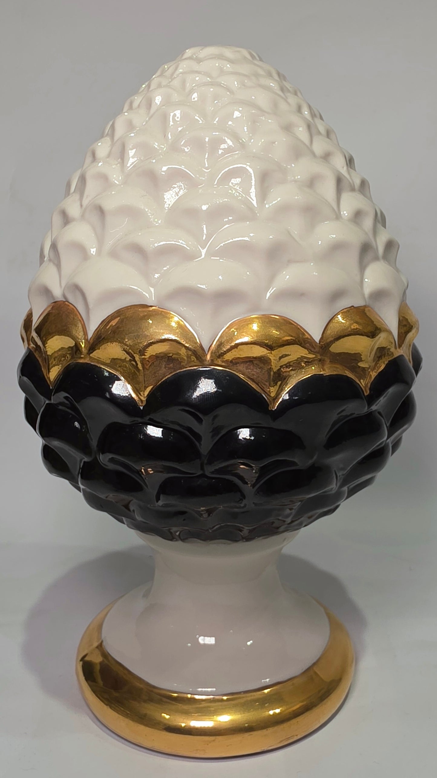 Pigna portafortuna in ceramica artigianale bicolore bianca e nera lucida, caratterizzata da una fascia centrale dorata che separa le squame in rilievo. Questo elegante oggetto ornamentale con base d'appoggio rifinita in oro è un complemento d'arredo di design ideale per donare un tocco di prestigio e tradizione siciliana agli ambienti contemporanei.