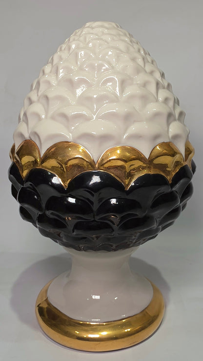 Pigna portafortuna in ceramica artigianale bicolore bianca e nera lucida, caratterizzata da una fascia centrale dorata che separa le squame in rilievo. Questo elegante oggetto ornamentale con base d'appoggio rifinita in oro è un complemento d'arredo di design ideale per donare un tocco di prestigio e tradizione siciliana agli ambienti contemporanei.