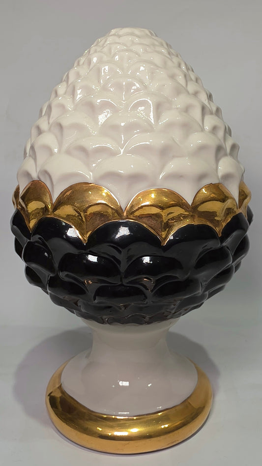 Pigna portafortuna in ceramica artigianale bicolore bianca e nera lucida, caratterizzata da una fascia centrale dorata che separa le squame in rilievo. Questo elegante oggetto ornamentale con base d'appoggio rifinita in oro è un complemento d'arredo di design ideale per donare un tocco di prestigio e tradizione siciliana agli ambienti contemporanei.