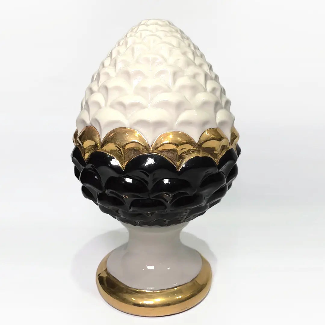 Pigna portafortuna in ceramica artigianale bicolore bianca e nera lucida, caratterizzata da una fascia centrale dorata che separa le squame in rilievo. Questo elegante oggetto ornamentale con base d'appoggio rifinita in oro è un complemento d'arredo di design ideale per donare un tocco di prestigio e tradizione siciliana agli ambienti contemporanei.