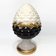 Pigna portafortuna in ceramica artigianale bicolore bianca e nera lucida, caratterizzata da una fascia centrale dorata che separa le squame in rilievo. Questo elegante oggetto ornamentale con base d'appoggio rifinita in oro è un complemento d'arredo di design ideale per donare un tocco di prestigio e tradizione siciliana agli ambienti contemporanei.