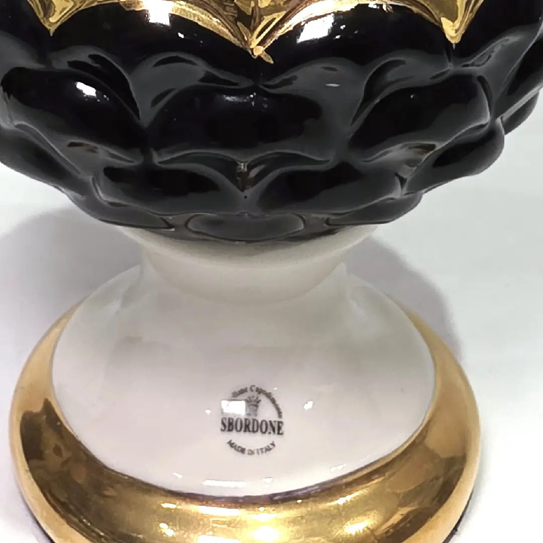 Pigna portafortuna in ceramica artigianale bicolore bianca e nera lucida, caratterizzata da una fascia centrale dorata che separa le squame in rilievo. Questo elegante oggetto ornamentale con base d'appoggio rifinita in oro è un complemento d'arredo di design ideale per donare un tocco di prestigio e tradizione siciliana agli ambienti contemporanei.