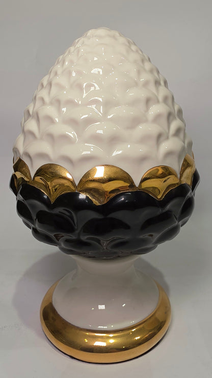 Pigna portafortuna in ceramica artigianale bicolore bianca e nera lucida, caratterizzata da una fascia centrale dorata che separa le squame in rilievo. Questo elegante oggetto ornamentale con base d'appoggio rifinita in oro è un complemento d'arredo di design ideale per donare un tocco di prestigio e tradizione siciliana agli ambienti contemporanei.