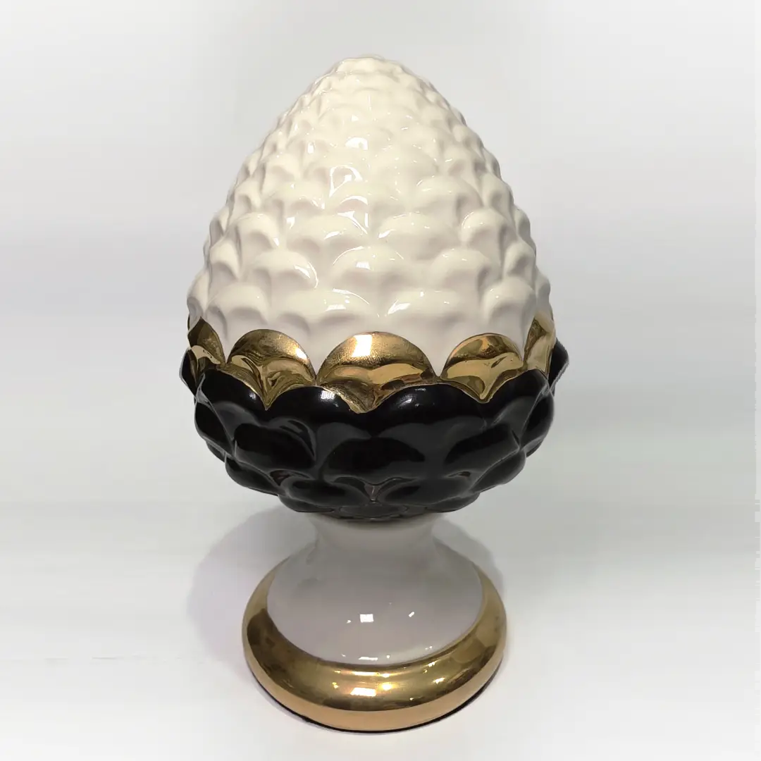 Pigna portafortuna in ceramica artigianale bicolore bianca e nera lucida, caratterizzata da una fascia centrale dorata che separa le squame in rilievo. Questo elegante oggetto ornamentale con base d'appoggio rifinita in oro è un complemento d'arredo di design ideale per donare un tocco di prestigio e tradizione siciliana agli ambienti contemporanei.