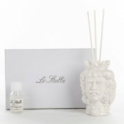 Profumatore d'ambiente in ceramica bianca lucida raffigurante una testa di moro maschile con corona e baffi, decorata con grappoli d'uva e foglie in rilievo, con bastoncini bianchi e boccetta di fragranza "Home Fragrance". Diffusore dalla tradizione siciliana firmato Le Stelle, presentato con la sua confezione bianca del marchio, ideale come idea regalo raffinata.