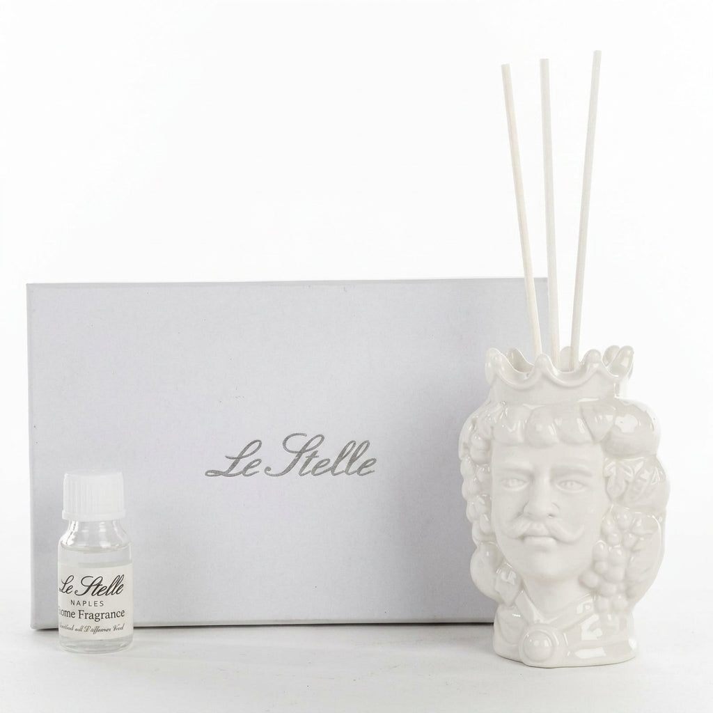 Profumatore d'ambiente in ceramica bianca lucida raffigurante una testa di moro maschile con corona e baffi, decorata con grappoli d'uva e foglie in rilievo, con bastoncini bianchi e boccetta di fragranza "Home Fragrance". Diffusore dalla tradizione siciliana firmato Le Stelle, presentato con la sua confezione bianca del marchio, ideale come idea regalo raffinata.