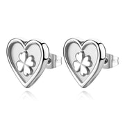 Orecchini a lobo S'agapò della collezione Duh Duh realizzati in acciaio anallergico con un design a forma di cuore dalla finitura lucida. Al centro di ogni cuore è presente un inserto satinato con un quadrifoglio portafortuna in rilievo finemente dettagliata. Gli orecchini sono dotati di una pratica chiusura a farfalla posteriore che garantisce una tenuta sicura e confortevole.