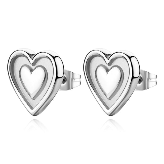Orecchini a lobo S'agapò della collezione Duh Duh realizzati in acciaio anallergico con un design a forma di cuore dalla finitura lucida. Al centro di ogni cuore è presente un inserto satinato con un cuore portafortuna in rilievo. Gli orecchini sono dotati di una pratica chiusura a farfalla posteriore che garantisce una tenuta sicura e confortevole.