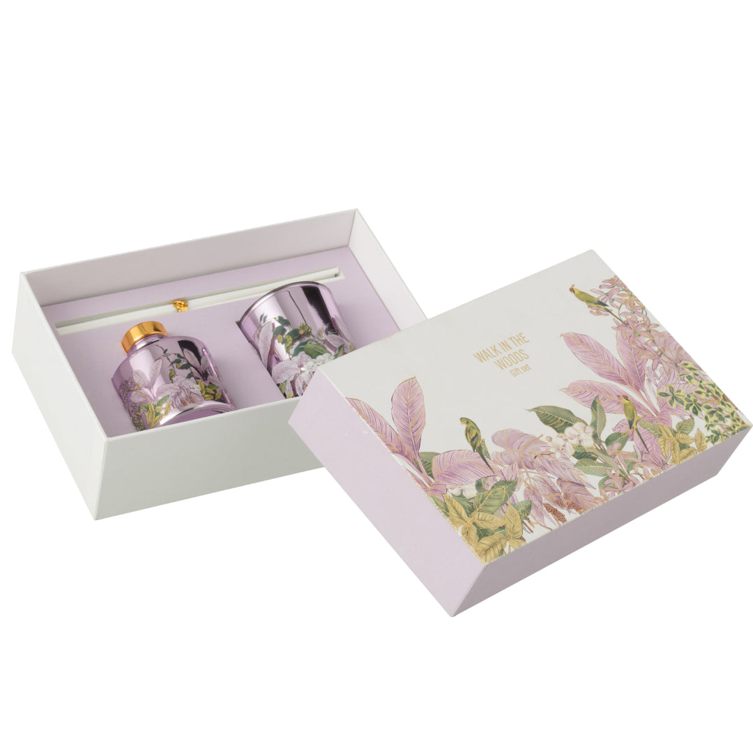 Il Set Regalo Candela e Diffusore Walk in the Woods Jolipa è un elegante cofanetto benessere che include una candela profumata e un diffusore di fragranza in vasi di vetro lilla con decorazioni botaniche. La confezione regalo raffinata con motivi di uccellini e foglie tropicali rosa rende questo kit perfetto per profumare la casa con stile o come pensiero speciale per l'home decor.