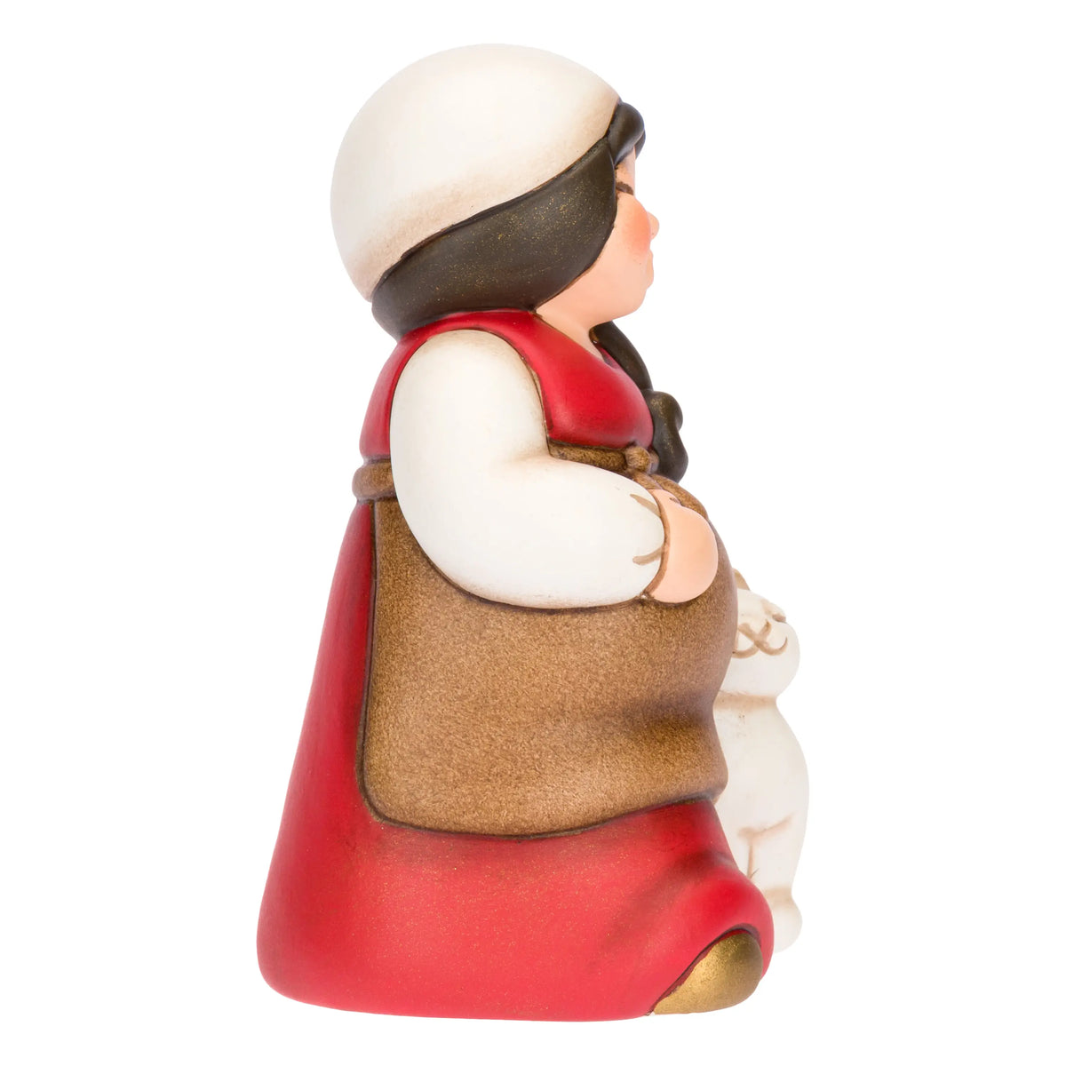 Statuina in ceramica raffigurante una pastorella del presepe in dolce attesa, con lunghi capelli scuri, veste rossa e mantello marrone, accanto a un agnellino bianco. Personaggio dal design classico e curato firmato THUN, ideale per arricchire il presepe o come idea regalo natalizia.