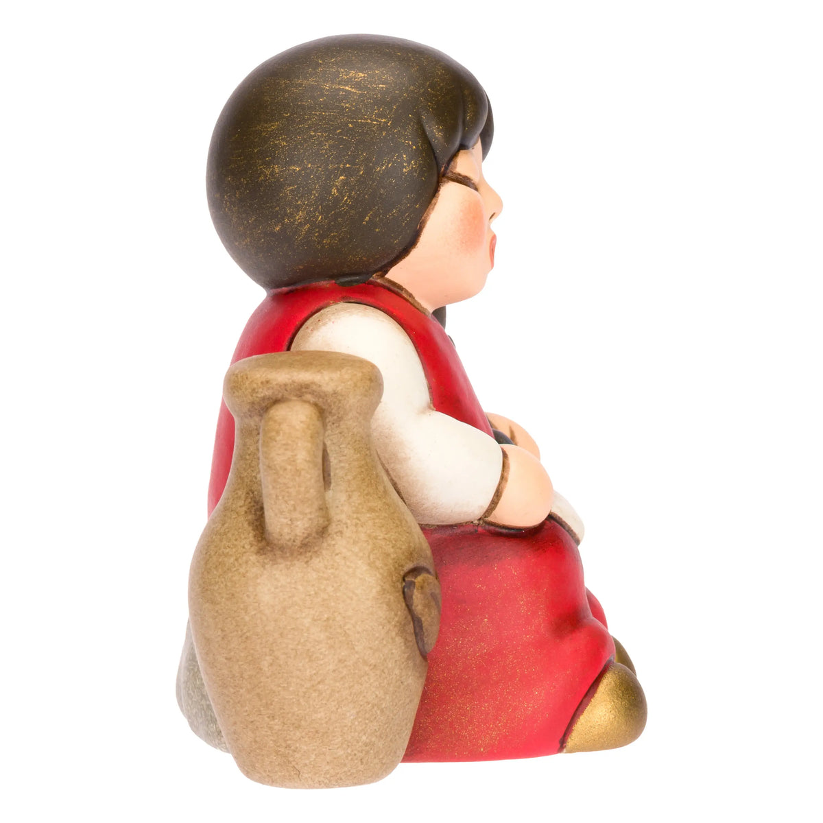 Statuina in ceramica raffigurante una bimba del presepe con treccia nera e vestito rosso e bianco, seduta accanto a un'anfora mentre raccoglie olive nel grembo. Personaggio dal design classico e curato firmato THUN, ideale per arricchire il presepe o come idea regalo natalizia.