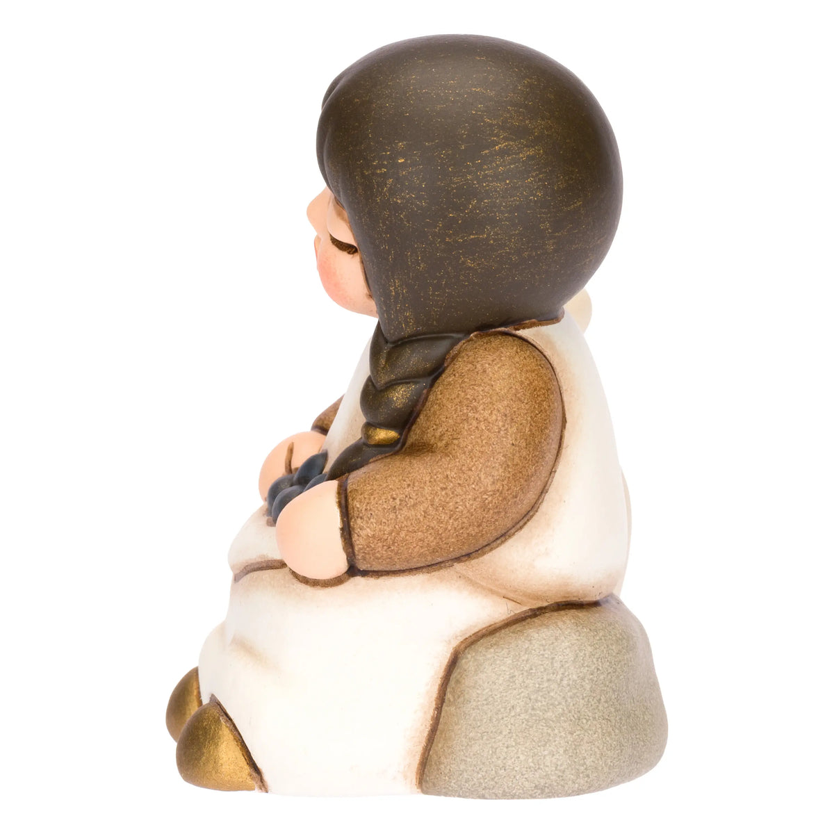 Statuina in ceramica raffigurante una bimba del presepe con treccia nera e vestito marrone e  bianco, seduta accanto a un'anfora mentre raccoglie olive nel grembo. Personaggio dal design classico e curato firmato THUN, ideale per arricchire il presepe o come idea regalo natalizia.
