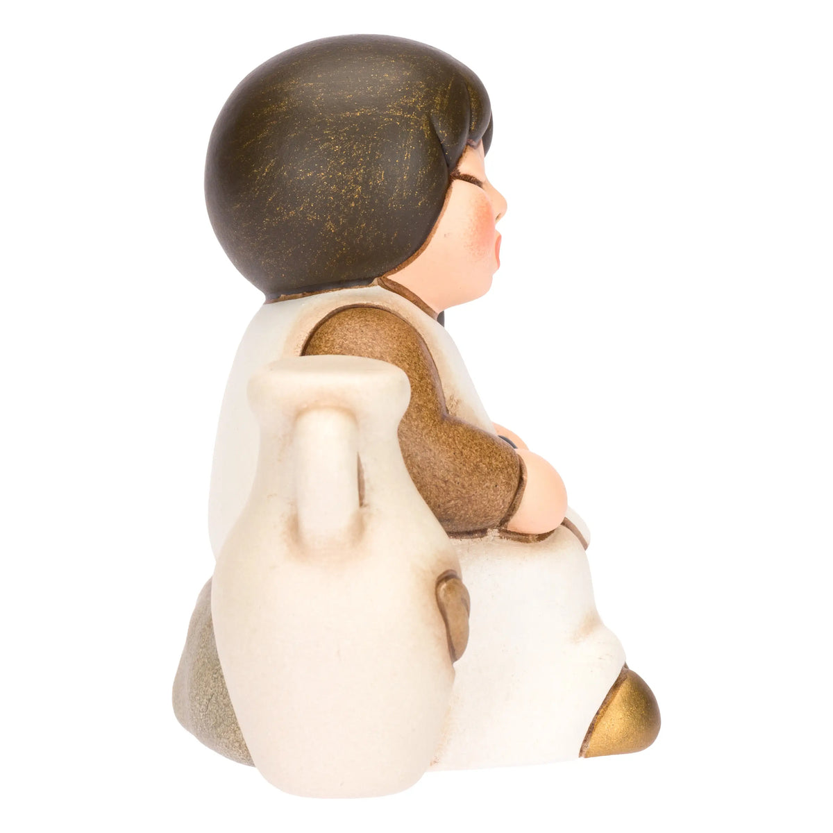 Statuina in ceramica raffigurante una bimba del presepe con treccia nera e vestito marrone e  bianco, seduta accanto a un'anfora mentre raccoglie olive nel grembo. Personaggio dal design classico e curato firmato THUN, ideale per arricchire il presepe o come idea regalo natalizia.
