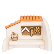 Miniatura in ceramica del presepe raffigurante la facciata di una casetta bianca con tetto in coppi arancioni, decorata con attrezzi da falegname dorati appesi e un vasetto di vernice sul davanzale. Ambientazione dal design classico e curato firmata THUN, ideale per arricchire la scenetta del falegname nel presepe o come idea regalo natalizia.