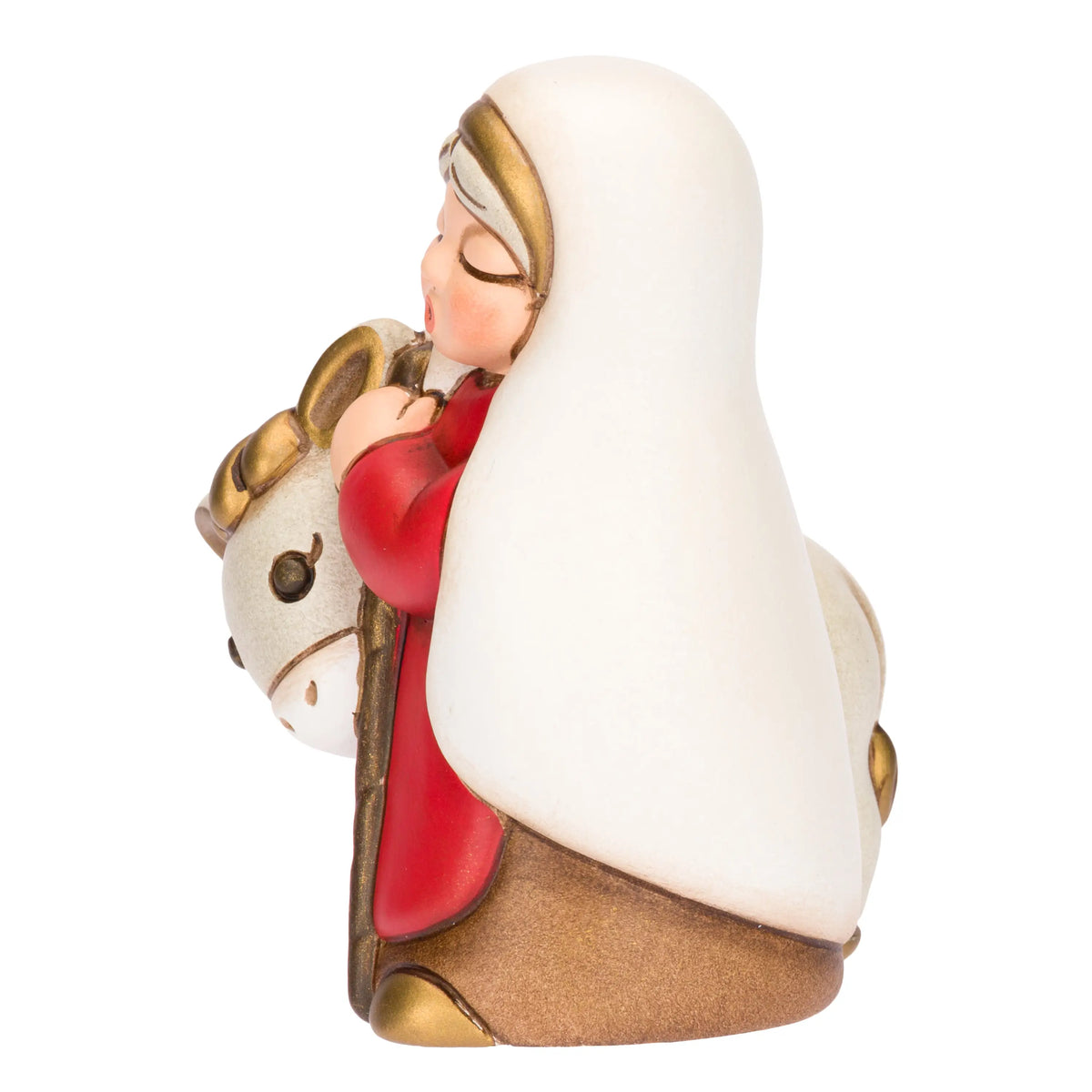 Statuina in ceramica raffigurante una donna del presepe con velo bianco e veste rossa, che accompagna un asinello con basto dorato appoggiando la mano sulla sua testa. Personaggio dal design classico e curato firmato THUN, ideale per arricchire il presepe o come idea regalo natalizia.