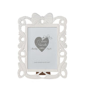 
Cornice portafoto rettangolare del marchio L'arte dei nacchi realizzata in resina bianca con una ricca lavorazione traforata in stile shabby chic lungo tutto il perimetro. Il design è caratterizzato da volute decorative e fregi ornamentali culminanti in un elegante fiocco centrale posto sulla parte superiore della cornice. Questo complemento d’arredo è ideale per esporre fotografie in ambienti dal gusto classico e romantico o come raffinata idea regalo per cerimonie ed eventi speciali.