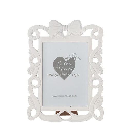 
Cornice portafoto rettangolare del marchio L'arte dei nacchi realizzata in resina bianca con una ricca lavorazione traforata in stile shabby chic lungo tutto il perimetro. Il design è caratterizzato da volute decorative e fregi ornamentali culminanti in un elegante fiocco centrale posto sulla parte superiore della cornice. Questo complemento d’arredo è ideale per esporre fotografie in ambienti dal gusto classico e romantico o come raffinata idea regalo per cerimonie ed eventi speciali.