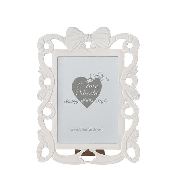 
Cornice portafoto rettangolare del marchio L'arte dei nacchi realizzata in resina bianca con una ricca lavorazione traforata in stile shabby chic lungo tutto il perimetro. Il design è caratterizzato da volute decorative e fregi ornamentali culminanti in un elegante fiocco centrale posto sulla parte superiore della cornice. Questo complemento d’arredo è ideale per esporre fotografie in ambienti dal gusto classico e romantico o come raffinata idea regalo per cerimonie ed eventi speciali.