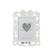 
Cornice portafoto rettangolare del marchio L'arte dei nacchi realizzata in resina bianca con una ricca lavorazione traforata in stile shabby chic lungo tutto il perimetro. Il design è caratterizzato da volute decorative e fregi ornamentali culminanti in un elegante fiocco centrale posto sulla parte superiore della cornice. Questo complemento d’arredo è ideale per esporre fotografie in ambienti dal gusto classico e romantico o come raffinata idea regalo per cerimonie ed eventi speciali.