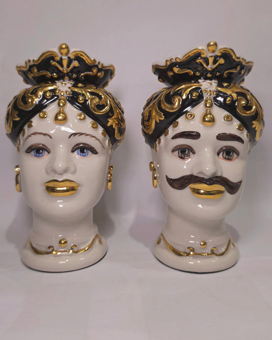 Coppia di Teste di Moro in ceramica artigianale bianca lucida con turbanti neri riccamente decorati da fregi e dettagli in oro zecchino. Queste sculture ornamentali raffiguranti un uomo con baffi e una donna con labbra dorate sono complementi d'arredo di lusso che reinterpretano la tradizione siciliana in chiave moderna ed elegante.