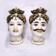 Coppia di Teste di Moro in ceramica artigianale bianca lucida con turbanti neri riccamente decorati da fregi e dettagli in oro zecchino. Queste sculture ornamentali raffiguranti un uomo con baffi e una donna con labbra dorate sono complementi d'arredo di lusso che reinterpretano la tradizione siciliana in chiave moderna ed elegante.