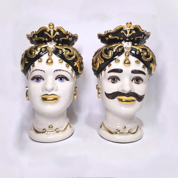 Coppia di Teste di Moro in ceramica artigianale bianca lucida con turbanti neri riccamente decorati da fregi e dettagli in oro zecchino. Queste sculture ornamentali raffiguranti un uomo con baffi e una donna con labbra dorate sono complementi d'arredo di lusso che reinterpretano la tradizione siciliana in chiave moderna ed elegante.