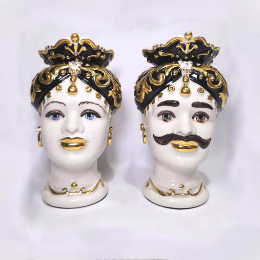 Coppia di Teste di Moro in ceramica artigianale bianca lucida con turbanti neri riccamente decorati da fregi e dettagli in oro zecchino. Queste sculture ornamentali raffiguranti un uomo con baffi e una donna con labbra dorate sono complementi d'arredo di lusso che reinterpretano la tradizione siciliana in chiave moderna ed elegante.