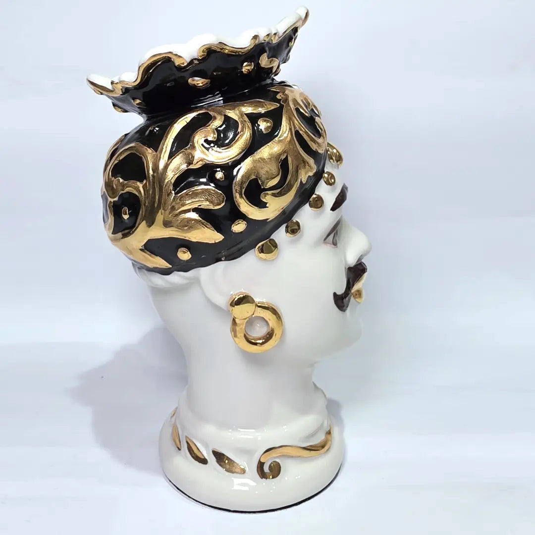 Coppia di Teste di Moro in ceramica artigianale bianca lucida con turbanti neri riccamente decorati da fregi e dettagli in oro zecchino. Queste sculture ornamentali raffiguranti un uomo con baffi e una donna con labbra dorate sono complementi d'arredo di lusso che reinterpretano la tradizione siciliana in chiave moderna ed elegante.