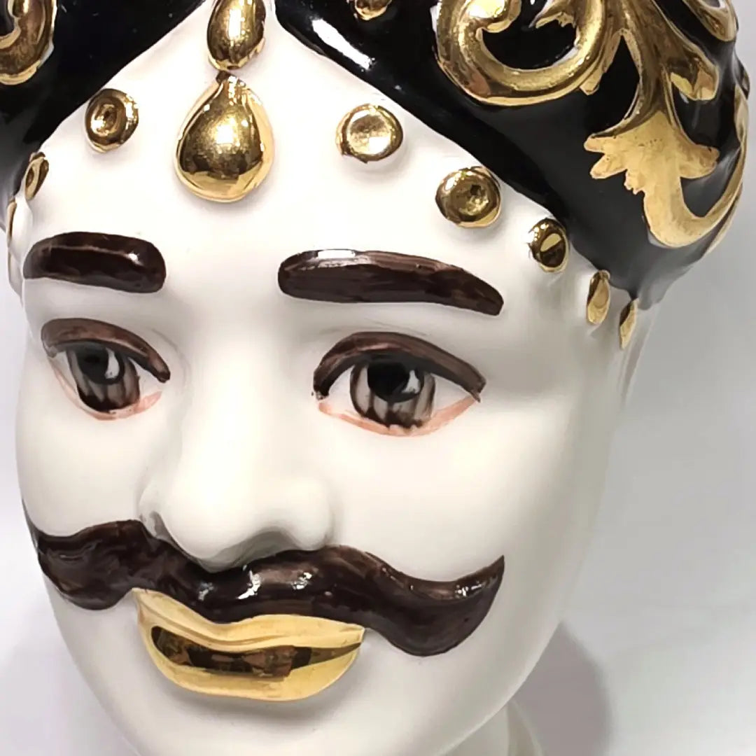 Coppia di Teste di Moro in ceramica artigianale bianca lucida con turbanti neri riccamente decorati da fregi e dettagli in oro zecchino. Queste sculture ornamentali raffiguranti un uomo con baffi e una donna con labbra dorate sono complementi d'arredo di lusso che reinterpretano la tradizione siciliana in chiave moderna ed elegante.