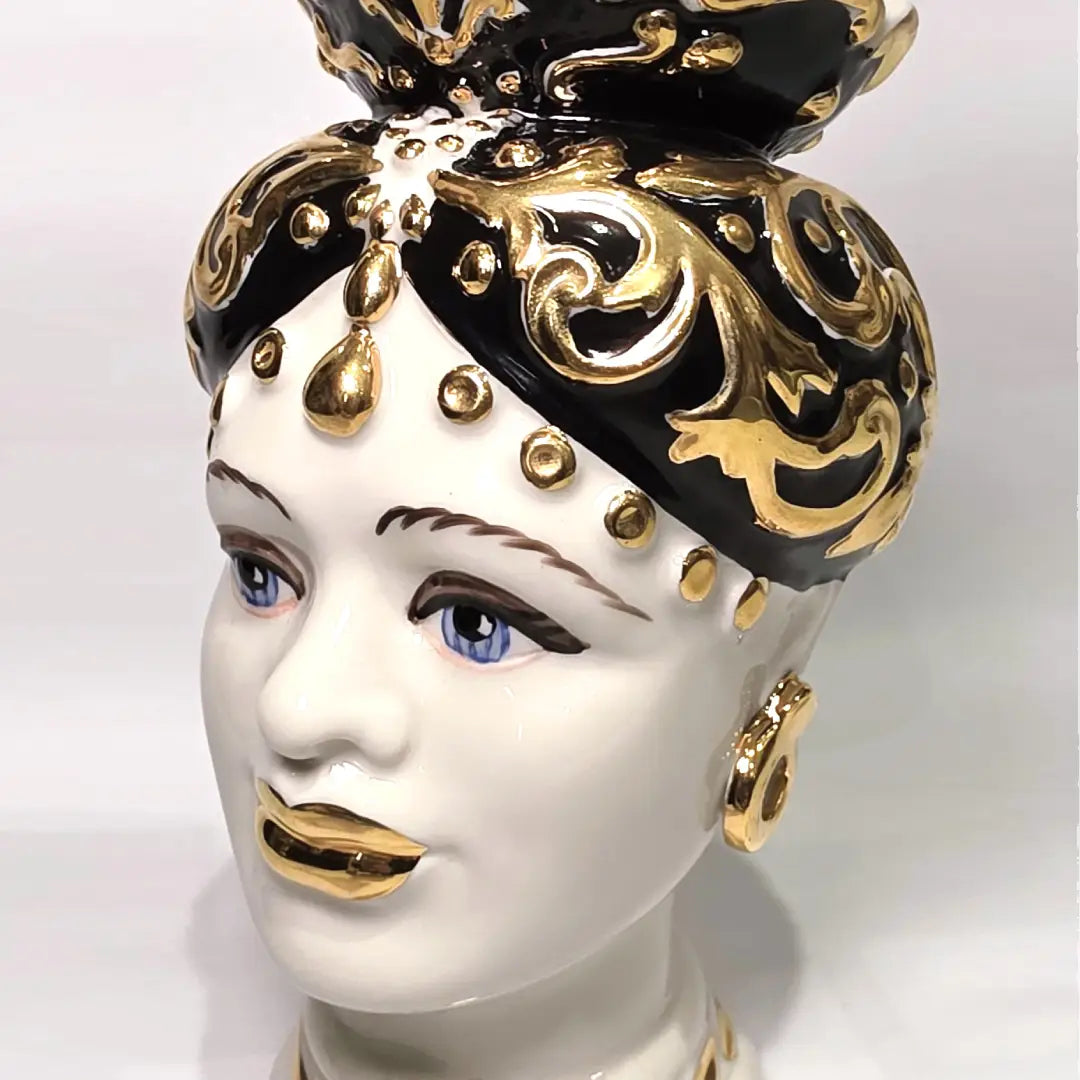 Coppia di Teste di Moro in ceramica artigianale bianca lucida con turbanti neri riccamente decorati da fregi e dettagli in oro zecchino. Queste sculture ornamentali raffiguranti un uomo con baffi e una donna con labbra dorate sono complementi d'arredo di lusso che reinterpretano la tradizione siciliana in chiave moderna ed elegante.