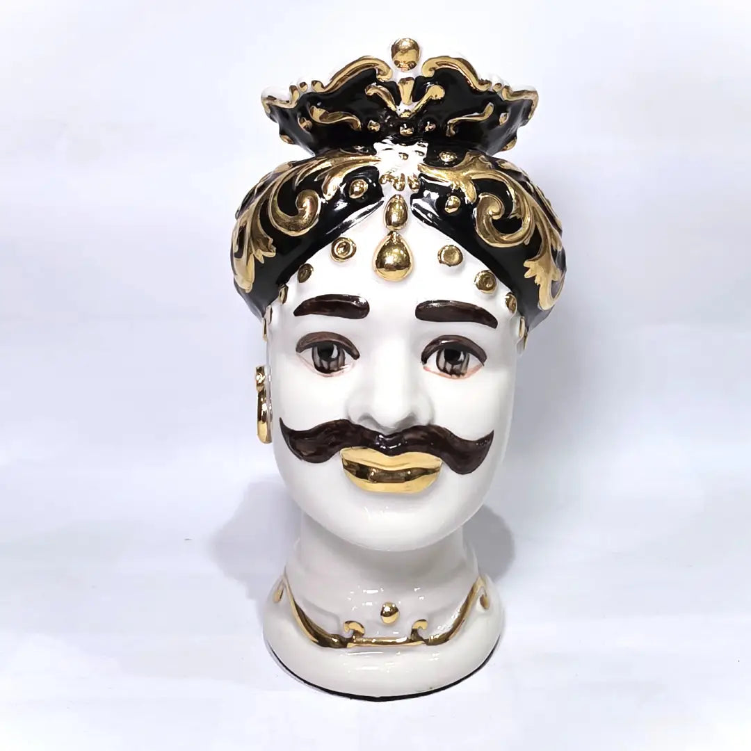Coppia di Teste di Moro in ceramica artigianale bianca lucida con turbanti neri riccamente decorati da fregi e dettagli in oro zecchino. Queste sculture ornamentali raffiguranti un uomo con baffi e una donna con labbra dorate sono complementi d'arredo di lusso che reinterpretano la tradizione siciliana in chiave moderna ed elegante.