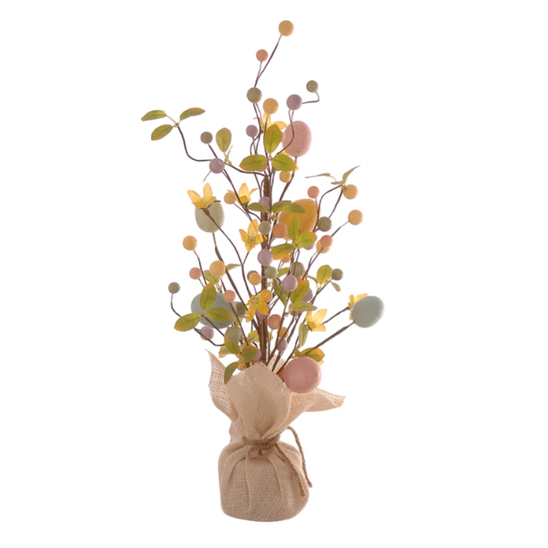 Statuina decorativa a forma di alberello pasquale slanciato. La base è avvolta in un sacchetto di juta color crema con chiusura a fiocco in spago. Dai rami sottili e alti si diramano uova pastello (rosa, azzurro, giallo), foglie verdi, piccoli fiori gialli e bacche decorative. Design verticale, ideale per composizioni floreali pasquali.