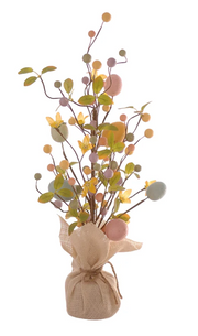 Statuina decorativa a forma di alberello pasquale slanciato. La base è avvolta in un sacchetto di juta color crema con chiusura a fiocco in spago. Dai rami sottili e alti si diramano uova pastello (rosa, azzurro, giallo), foglie verdi, piccoli fiori gialli e bacche decorative. Design verticale, ideale per composizioni floreali pasquali.
