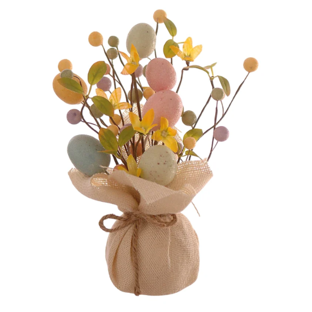 Statuina decorativa pasquale a forma di piccolo alberello o bouquet. La base è costituita da un sacchetto in tela di juta color crema, chiuso da un cordino in spago naturale. Dal sacchetto si sprigionano rami sottili decorati con uova di Pasqua in tonalità pastello (rosa, azzurro e giallo), piccoli fiori gialli e bacche coordinate. Design rustico e primaverile.