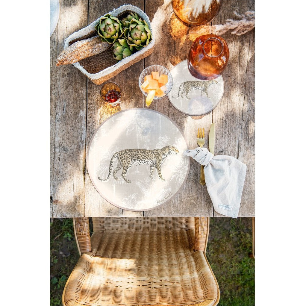 Tovaglietta americana rotonda in vinile della collezione "Leopard" di Blanc Mariclo' caratterizzata dall'illustrazione realistica di un leopardo maculato in posizione di profilo. Lo sfondo beige presenta un delicato motivo esotico con palme e piante tropicali stilizzate in bianco, ideale per apparecchiare una tavola moderna e grintosa dal tocco jungle chic.