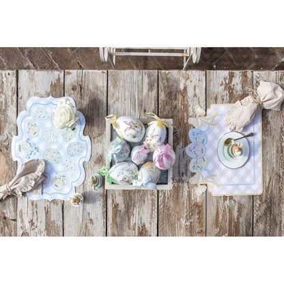 Tovaglietta americana in vinile della collezione "Pretty Easter" firmata Blanc Mariclo' con un motivo a scacchi bianchi e rosa perfetto per la colazione o il pranzo pasquale. La tovaglietta sagomata è decorata sul bordo superiore con fiocchi gialli e tre uova di Pasqua colorate nei toni pastello con dettagli floreali azzurri.